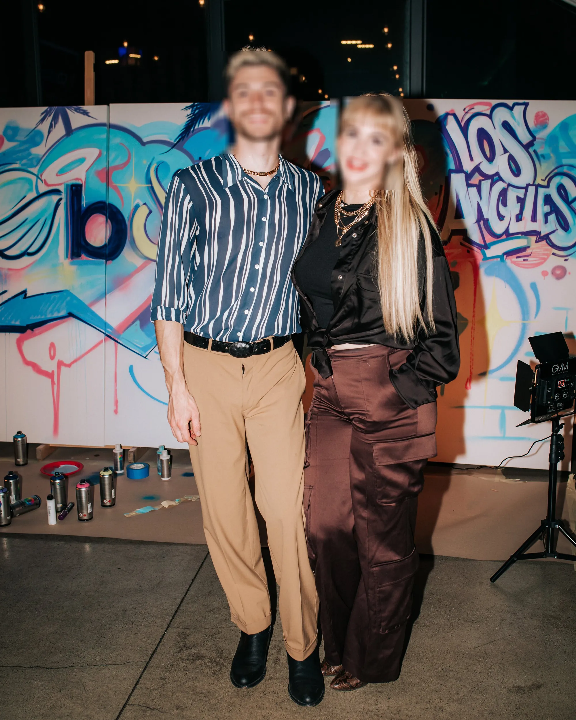 Two guests posing in front of the live-painted graffiti panels at the BonFire Ventures afterparty in Los Angeles, with spray cans lined up on the floor