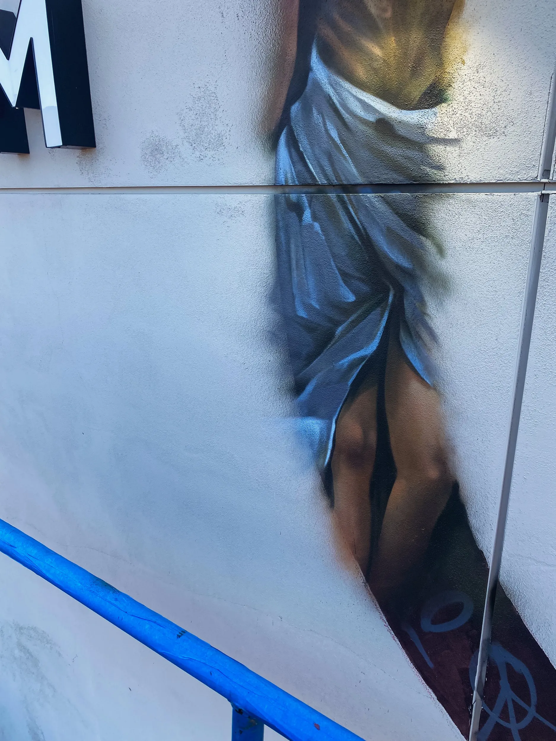 Detailed mural of a woman in a blue dress with an exposed leg, painted on a white wall.