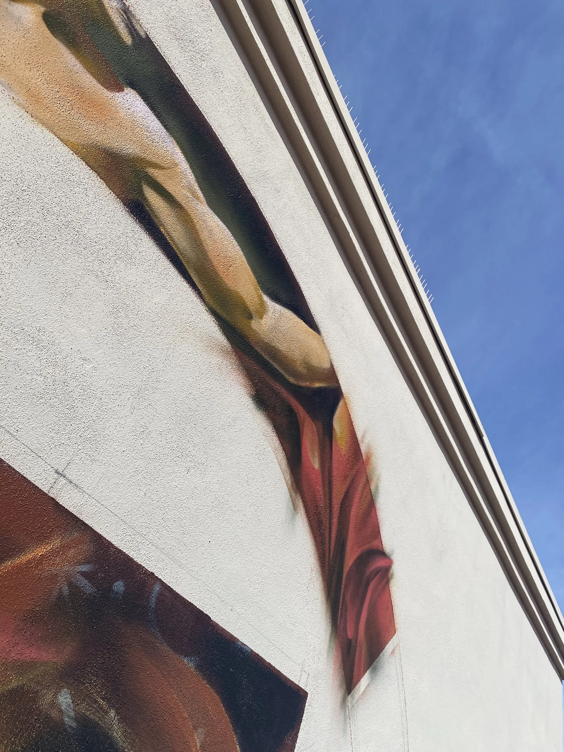 Close-up view of a colorful mural painted on an exterior wall of a building, with the blue sky visible at the top.