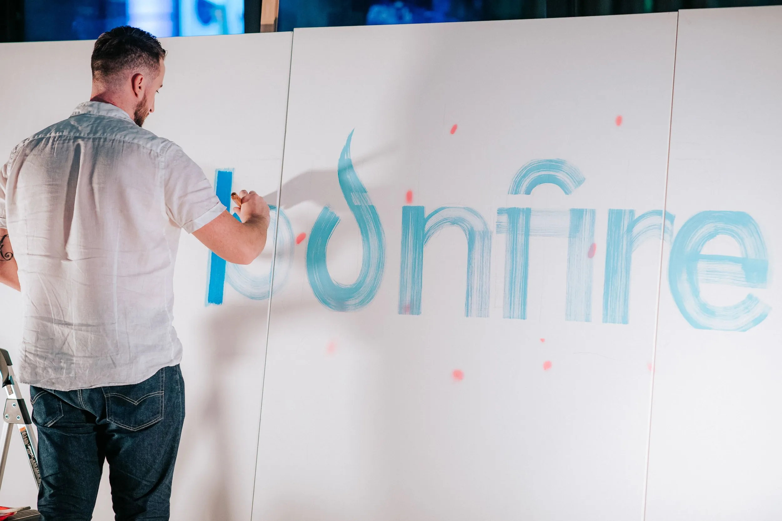Pezer97 hand-painting the Bonfire wordmark in blue brush strokes across white panels during the BonFire Ventures live painting event